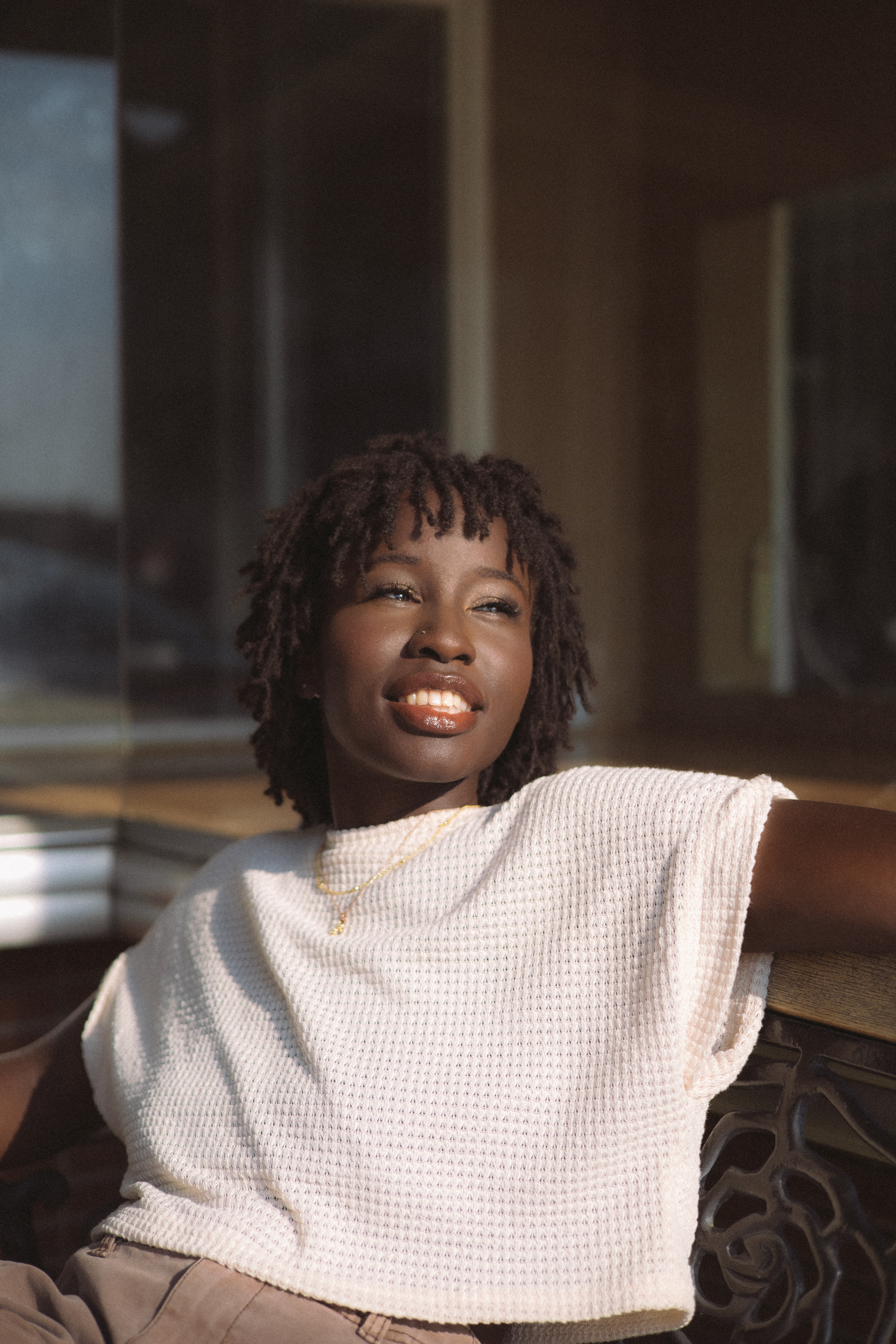 Young woman with dreadlocks smiles warmly in soft natural light, outdoor portrait