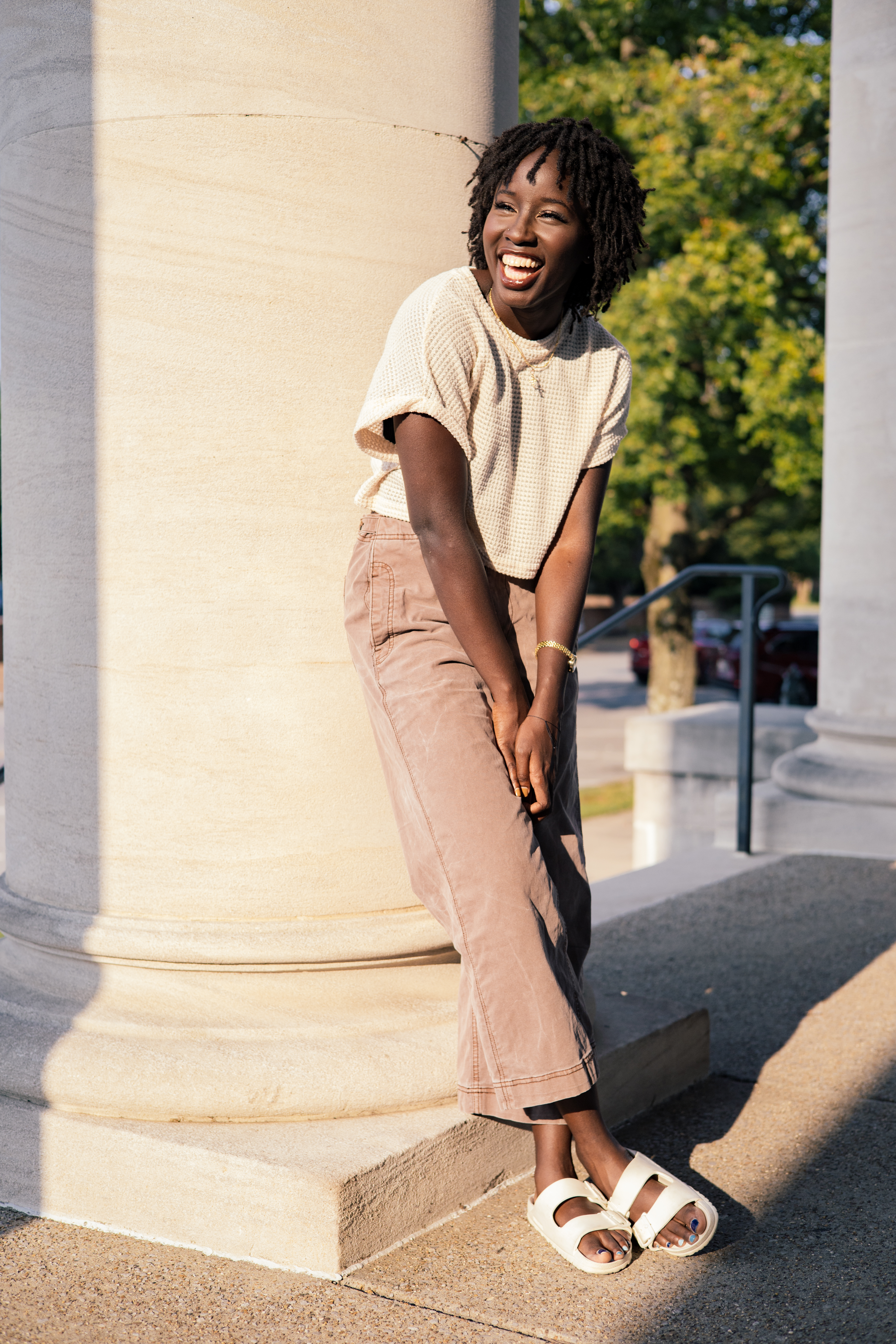 Joyful young woman laughs while leaning against a stone column outdoors
