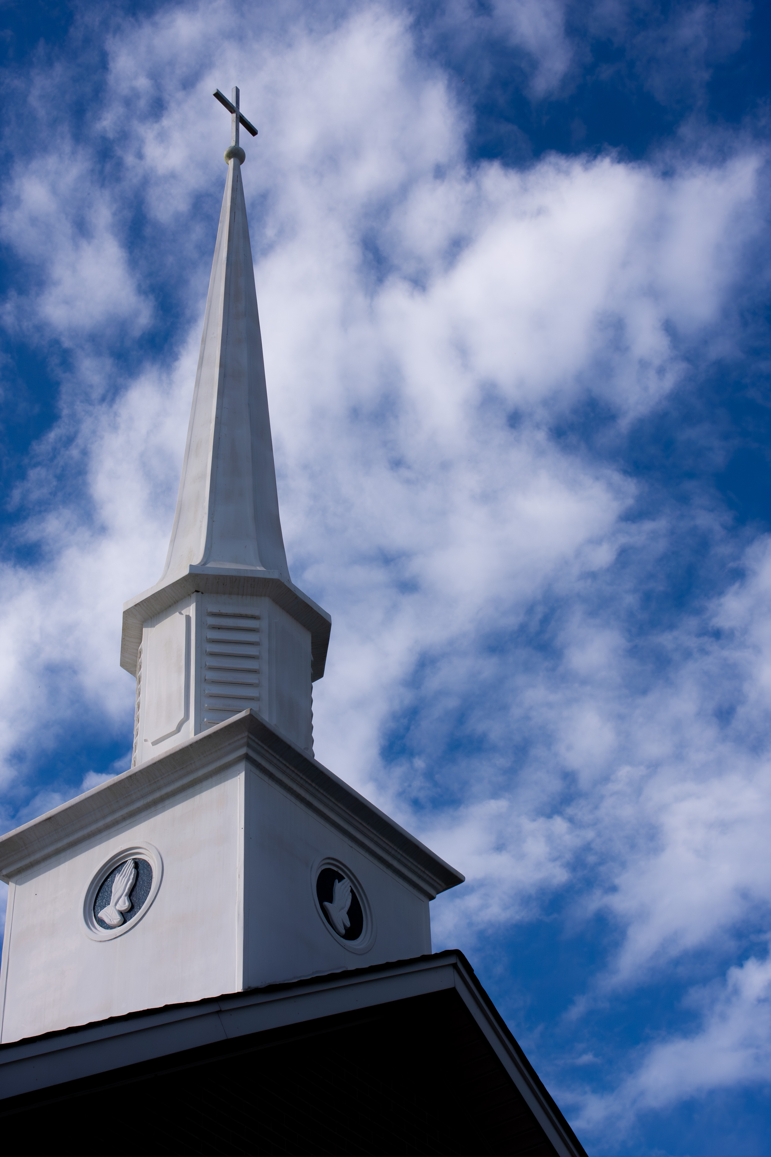 White church steeple with a cross against a bright blue sky with clouds