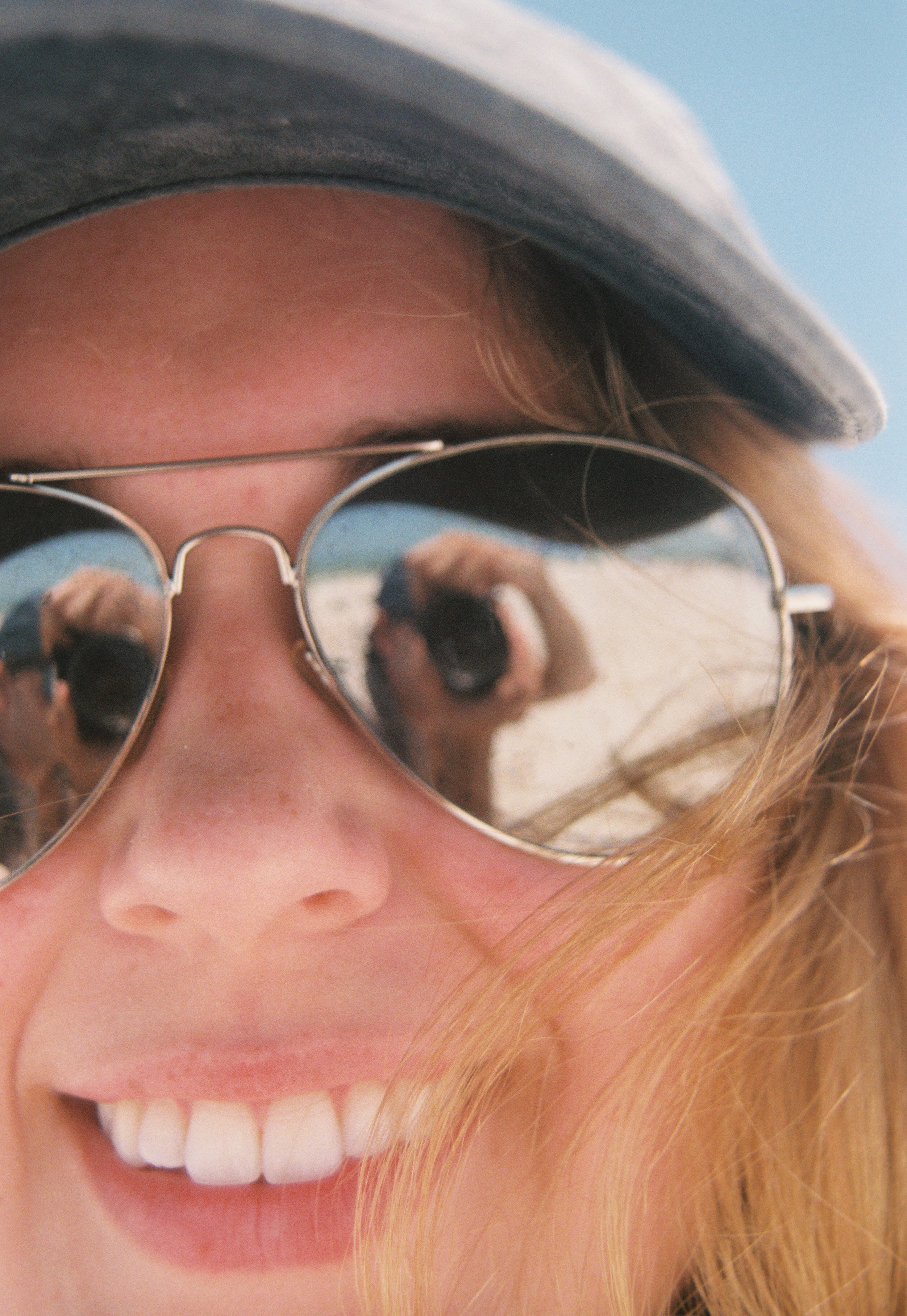 Close-up portrait of a smiling woman wearing sunglasses and a hat on a beach