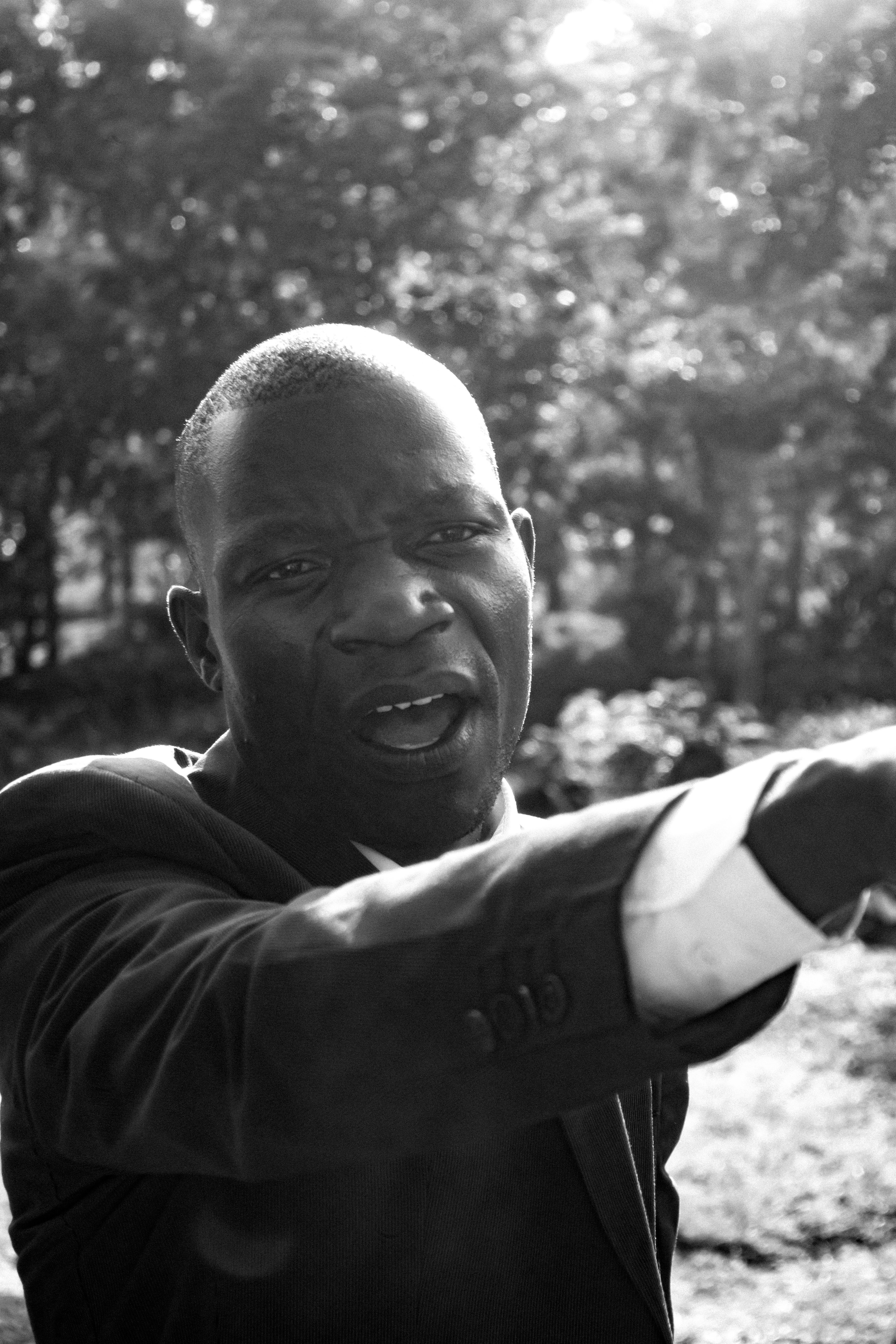 Man in suit pointing assertively outdoors with trees in the background