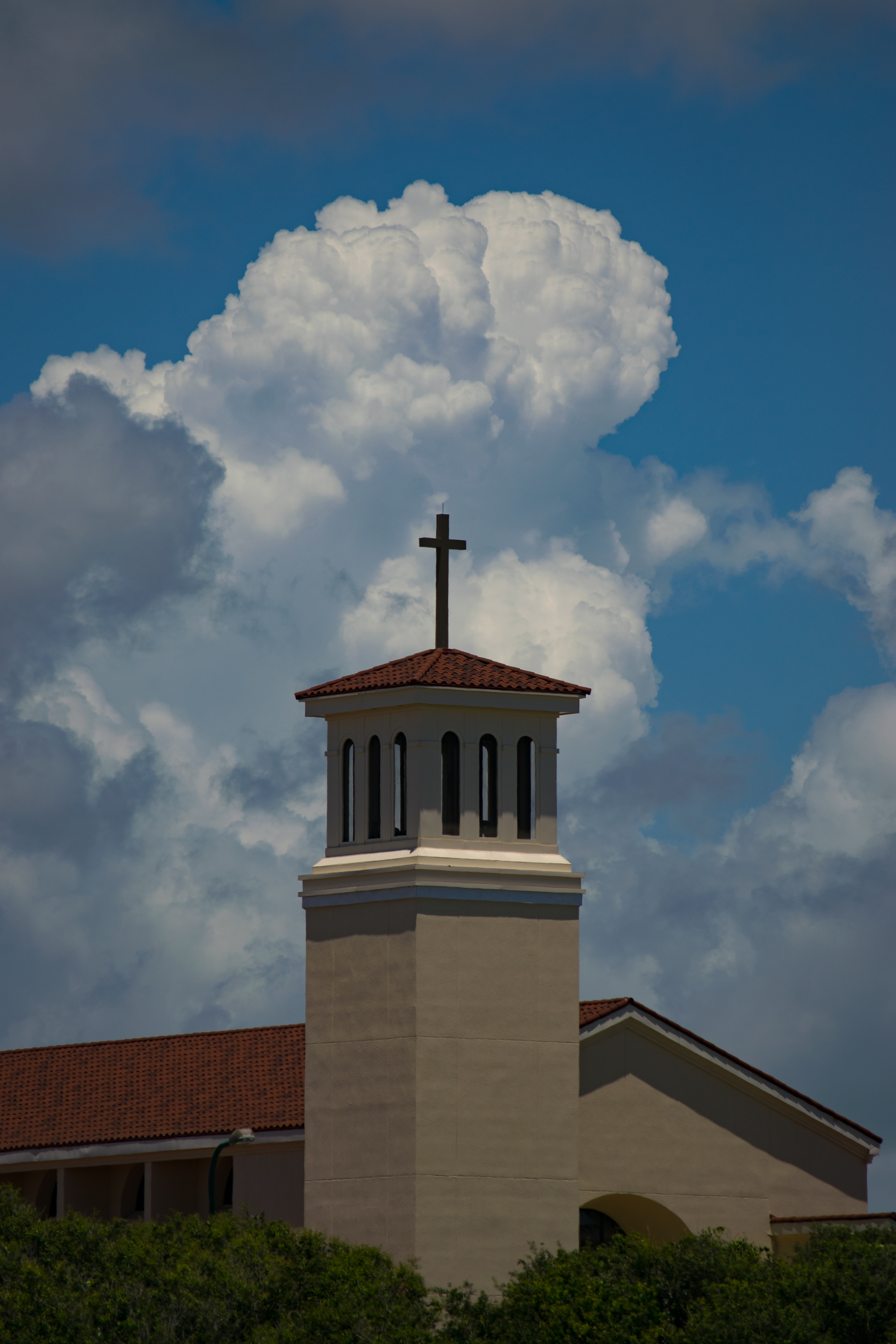 Church bell tower with cross against a dramatic sky and fluffy clouds