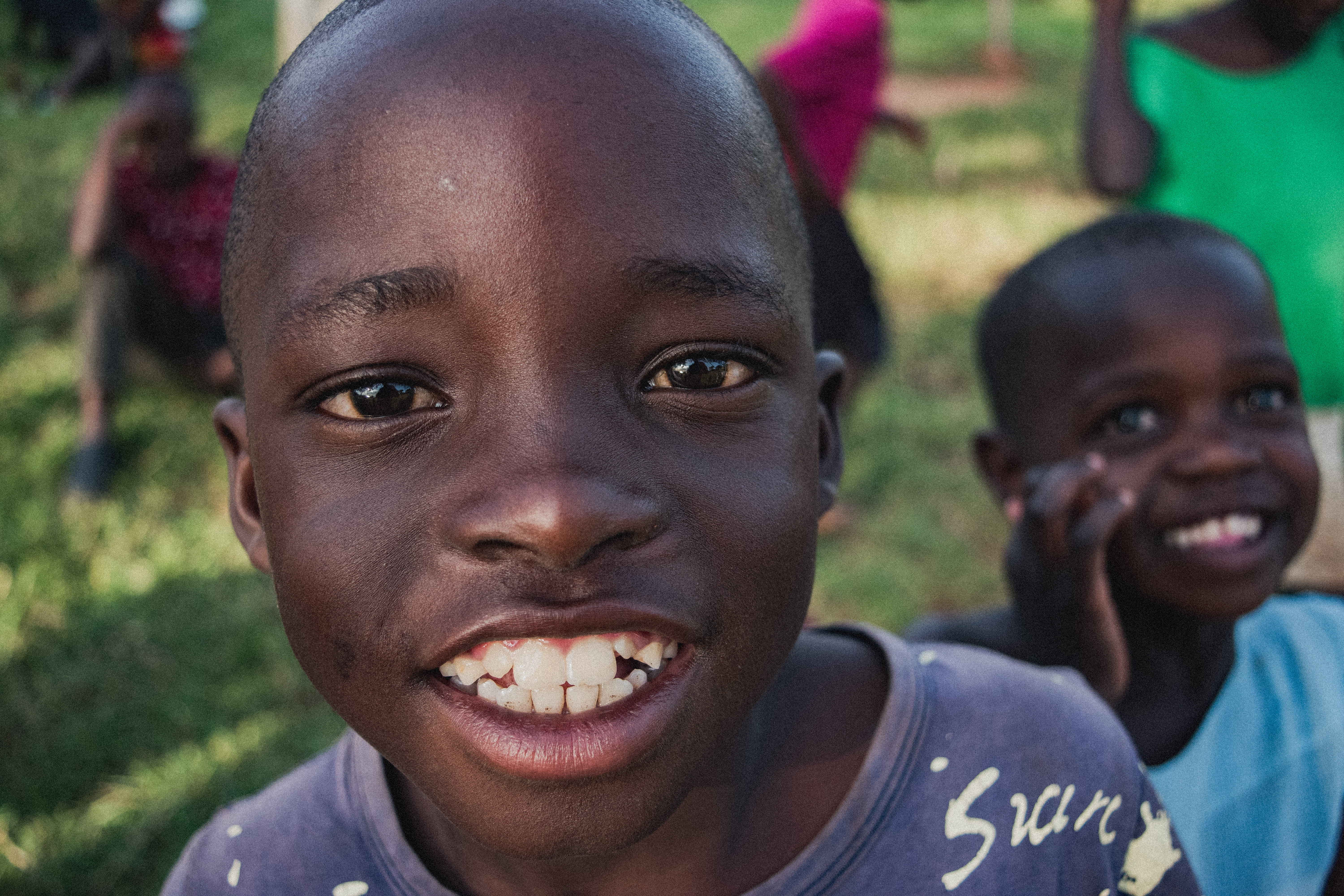 Close-up portrait of a smiling boy with other children blurred in the background outdoors