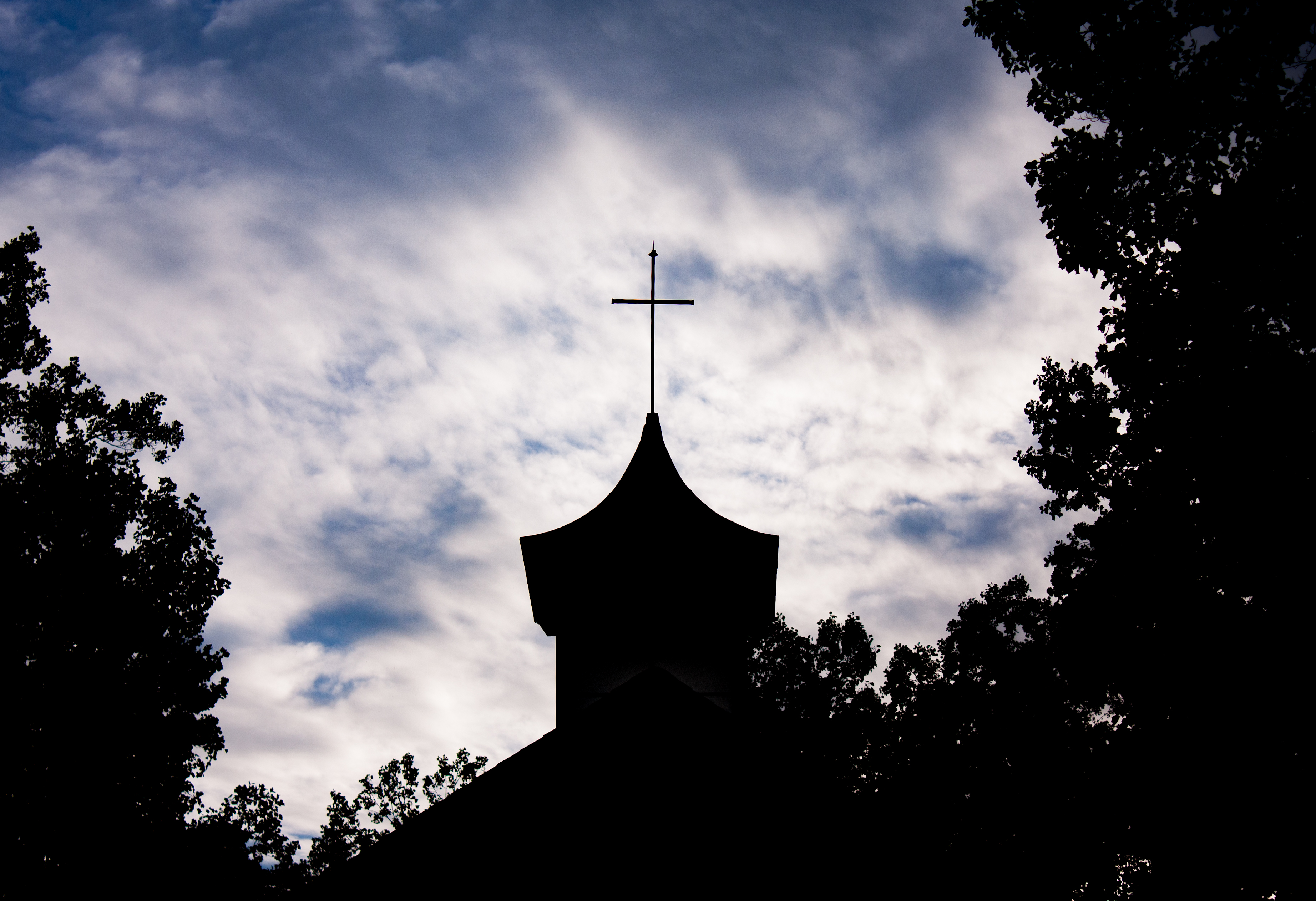 Silhouette of a church steeple with a cross against a cloudy sky