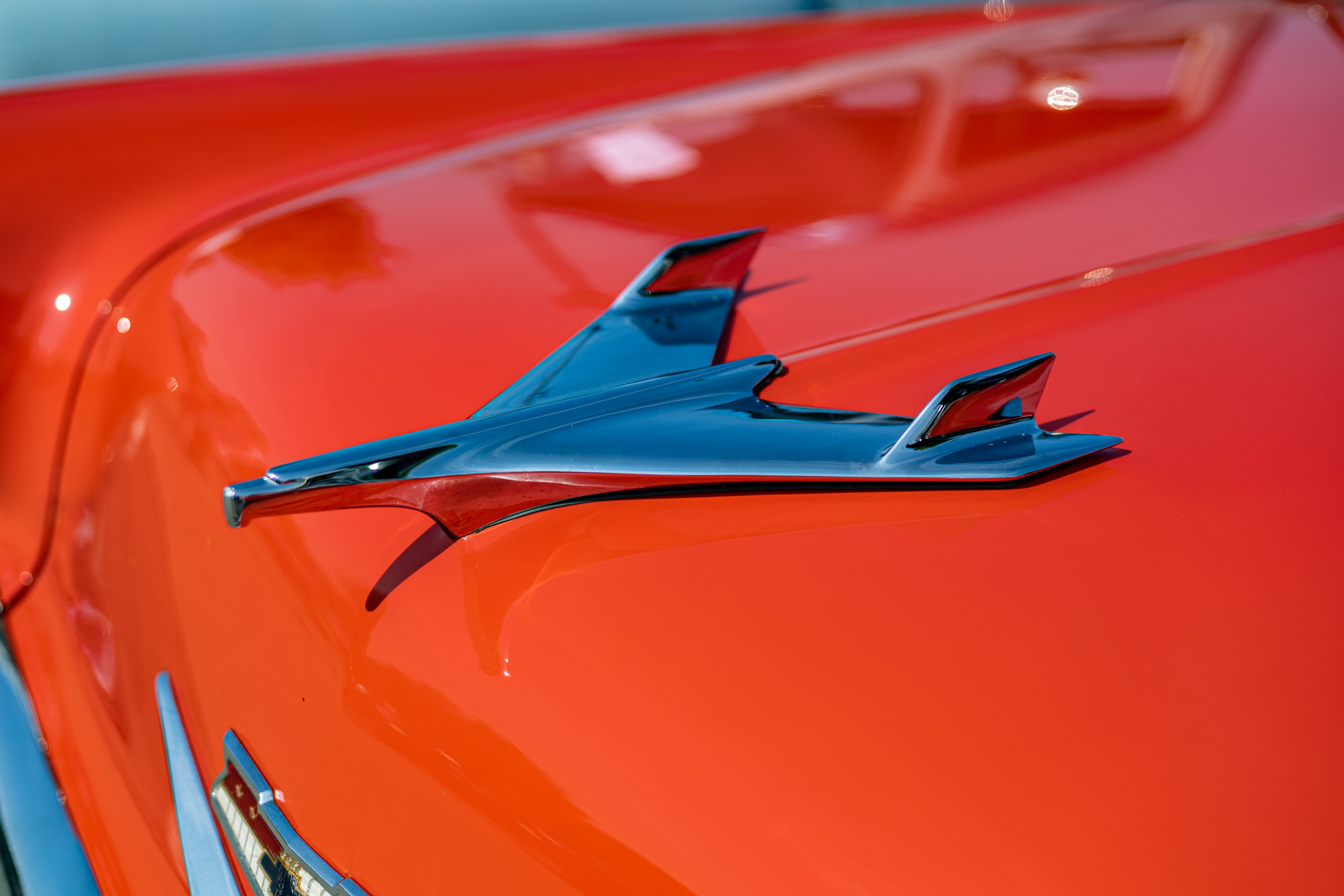 Chrome hood ornament on a shiny orange vintage car under bright sunlight