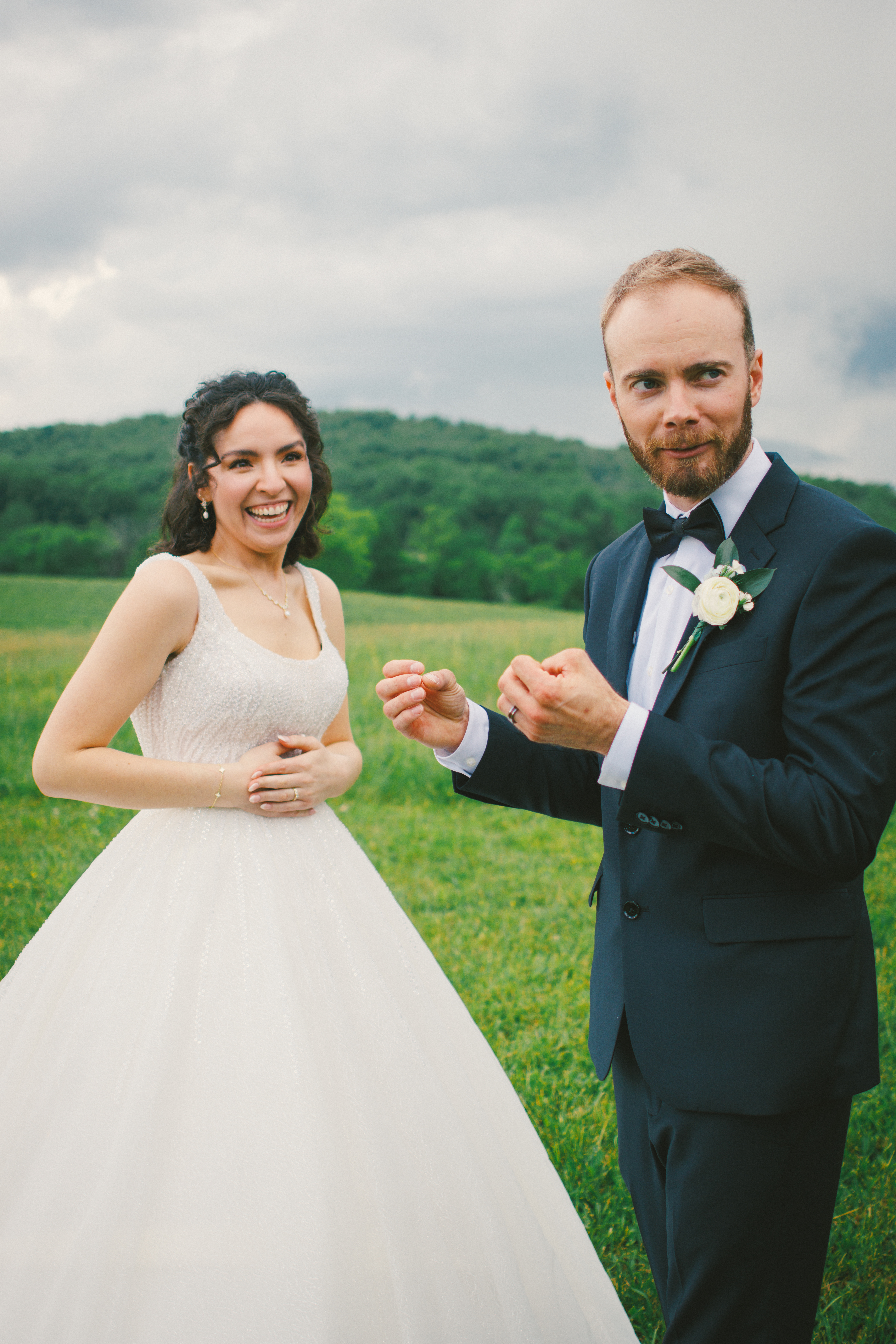 Joyful bride and groom in a field on their wedding day with rolling hills behind them