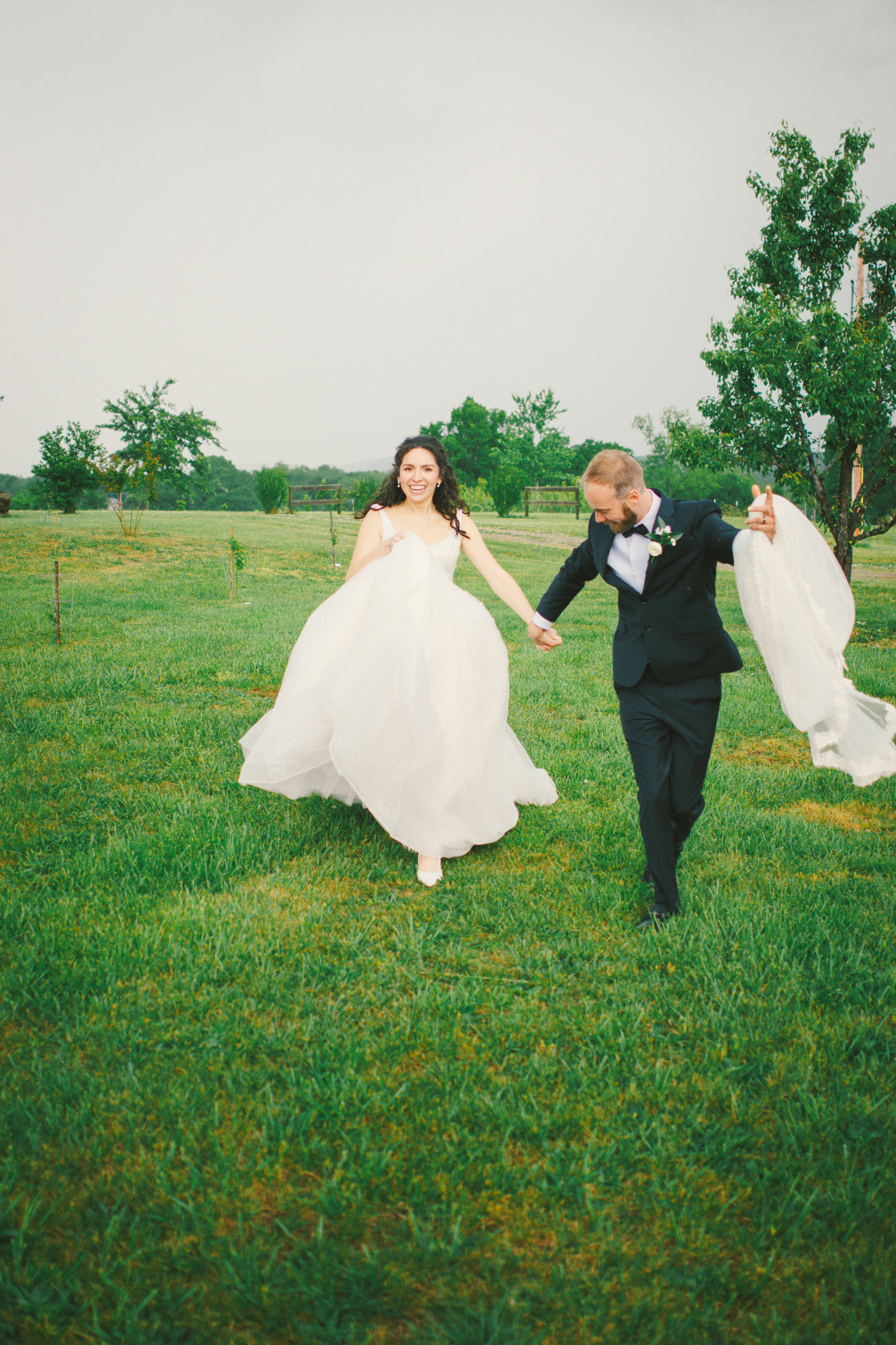 Joyful bride and groom running hand-in-hand across a grassy field during their wedding day
