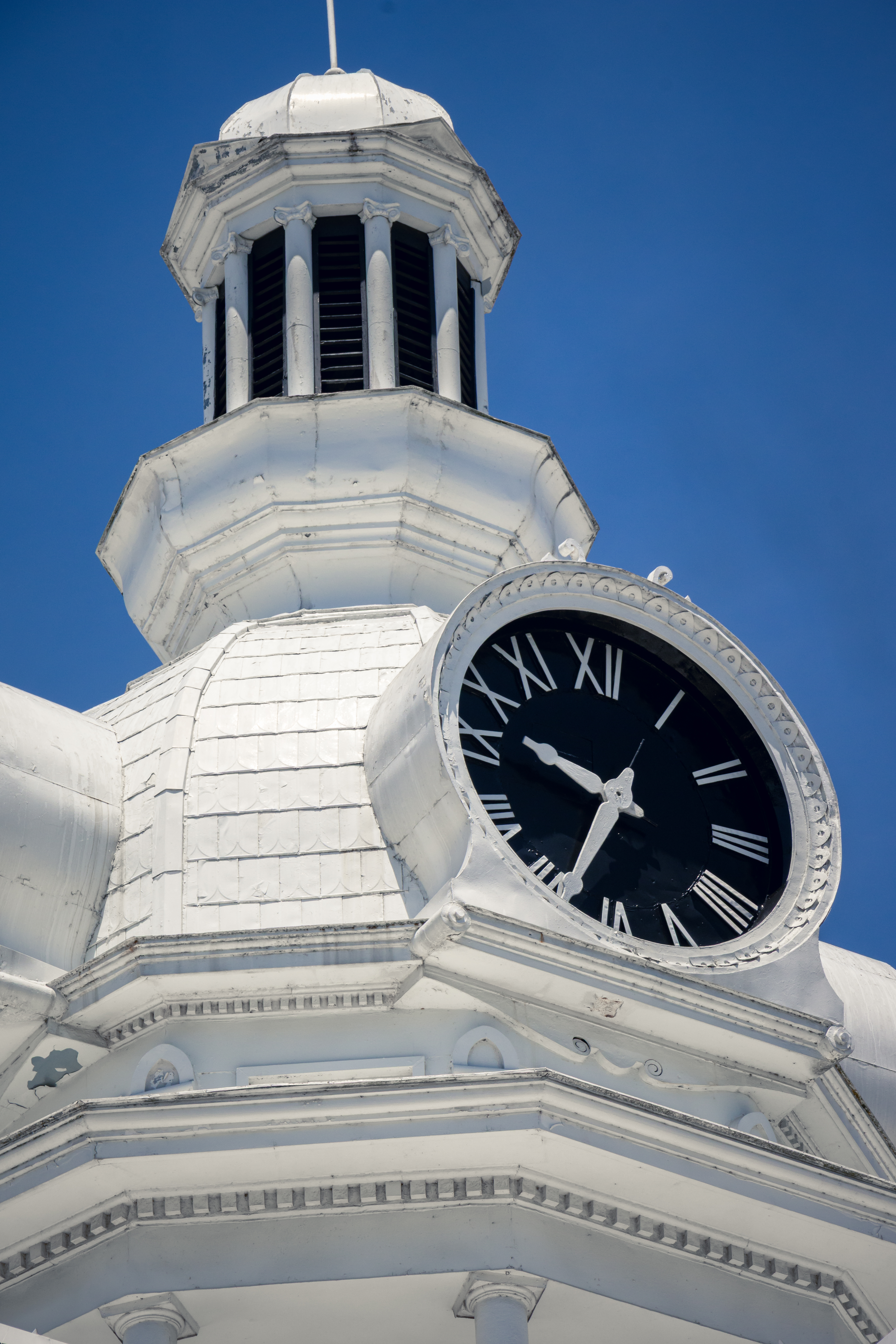 White clock tower with Roman numerals against a bright blue sky