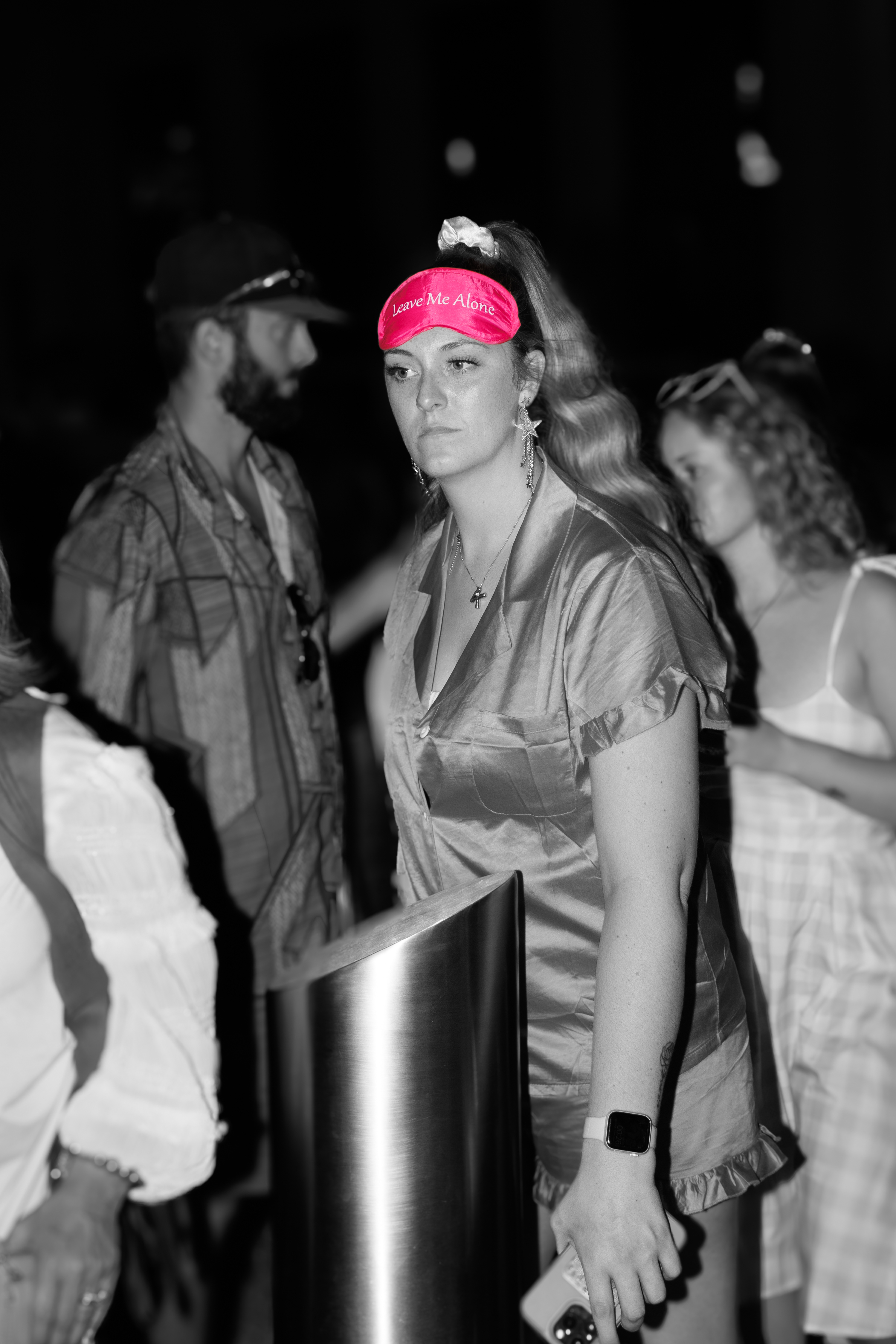 Woman in pajamas and sleep mask stands with others at night