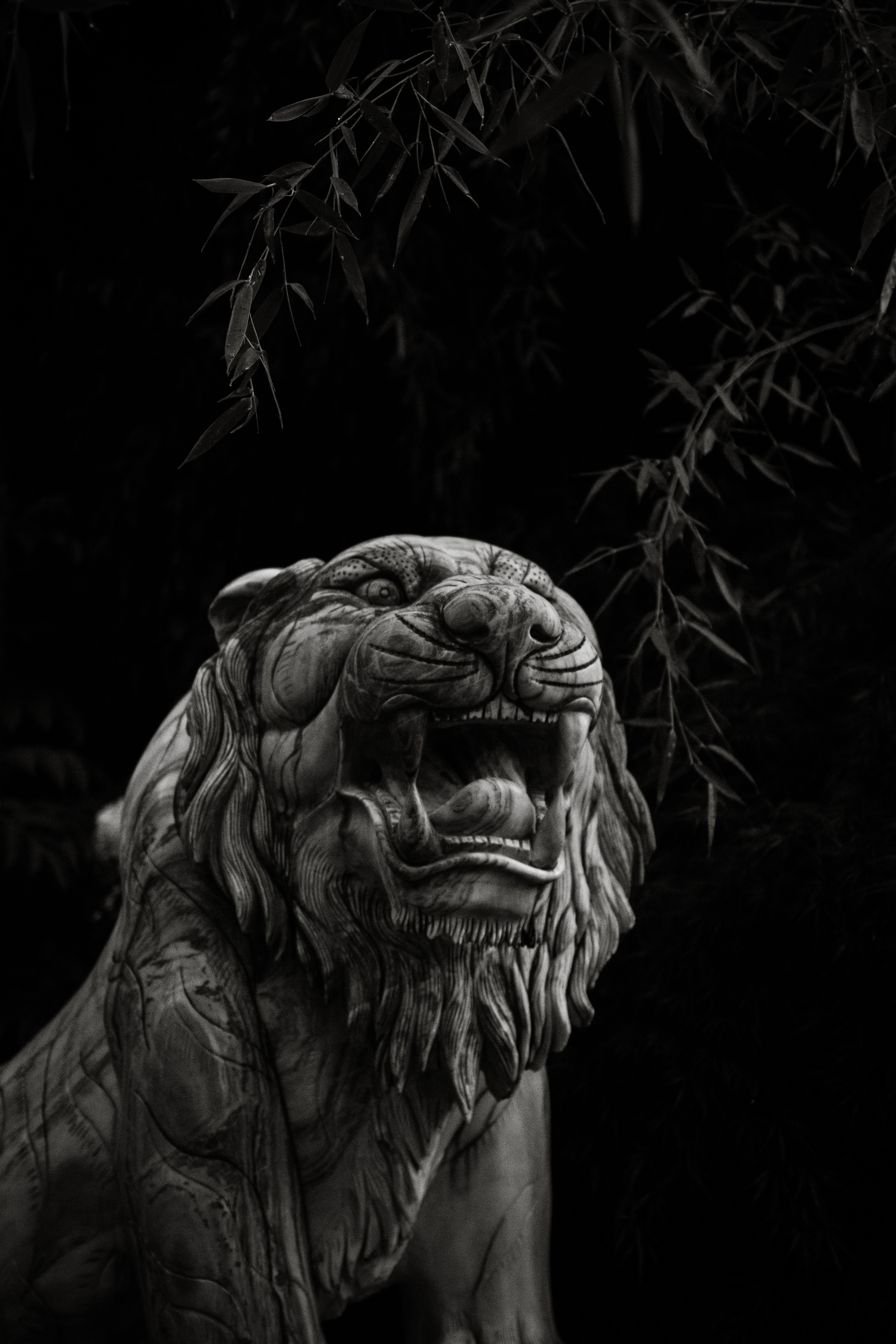 Stone tiger statue with open mouth and bamboo branches against a dark background