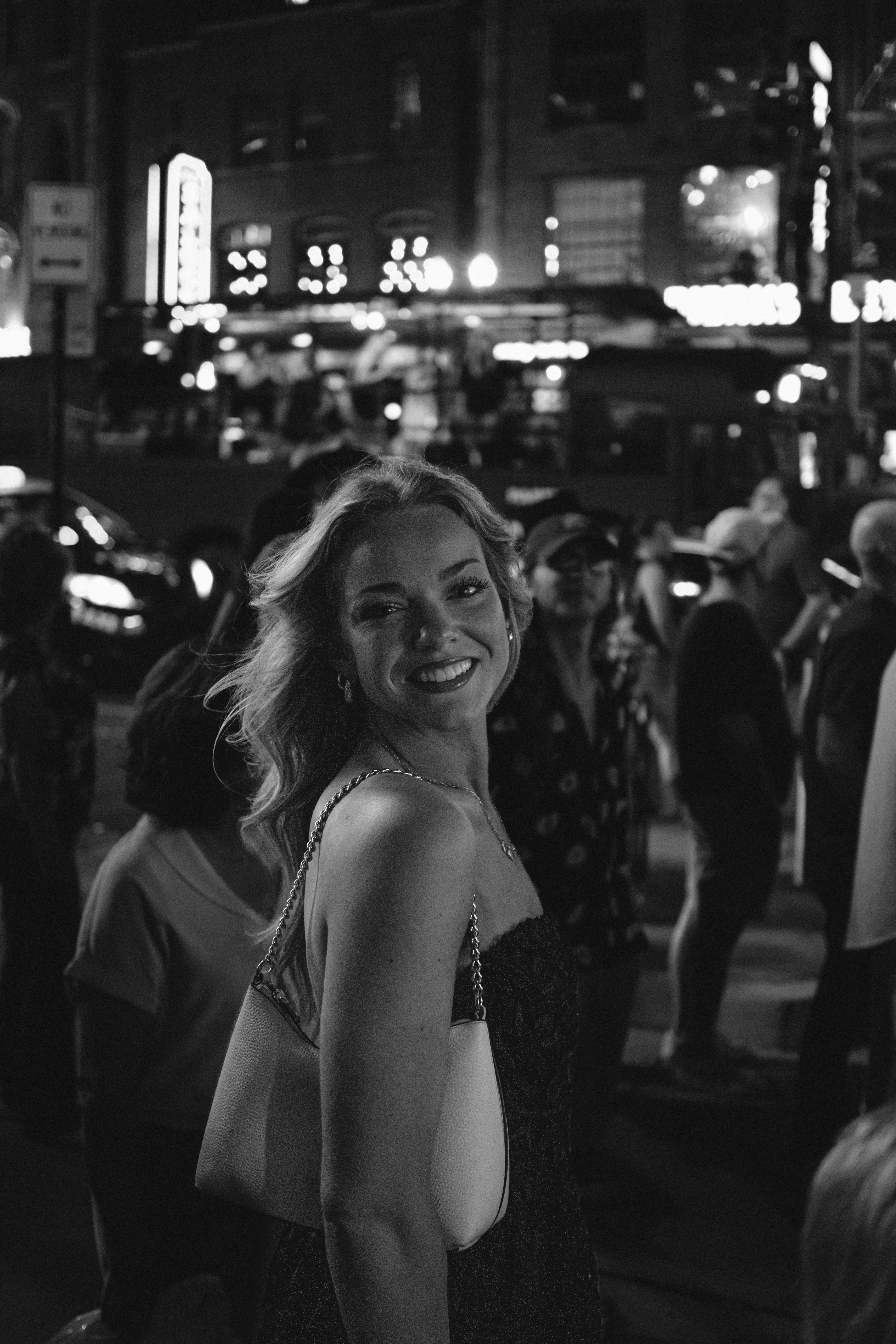 Smiling woman with blonde hair in a crowd at night with city lights