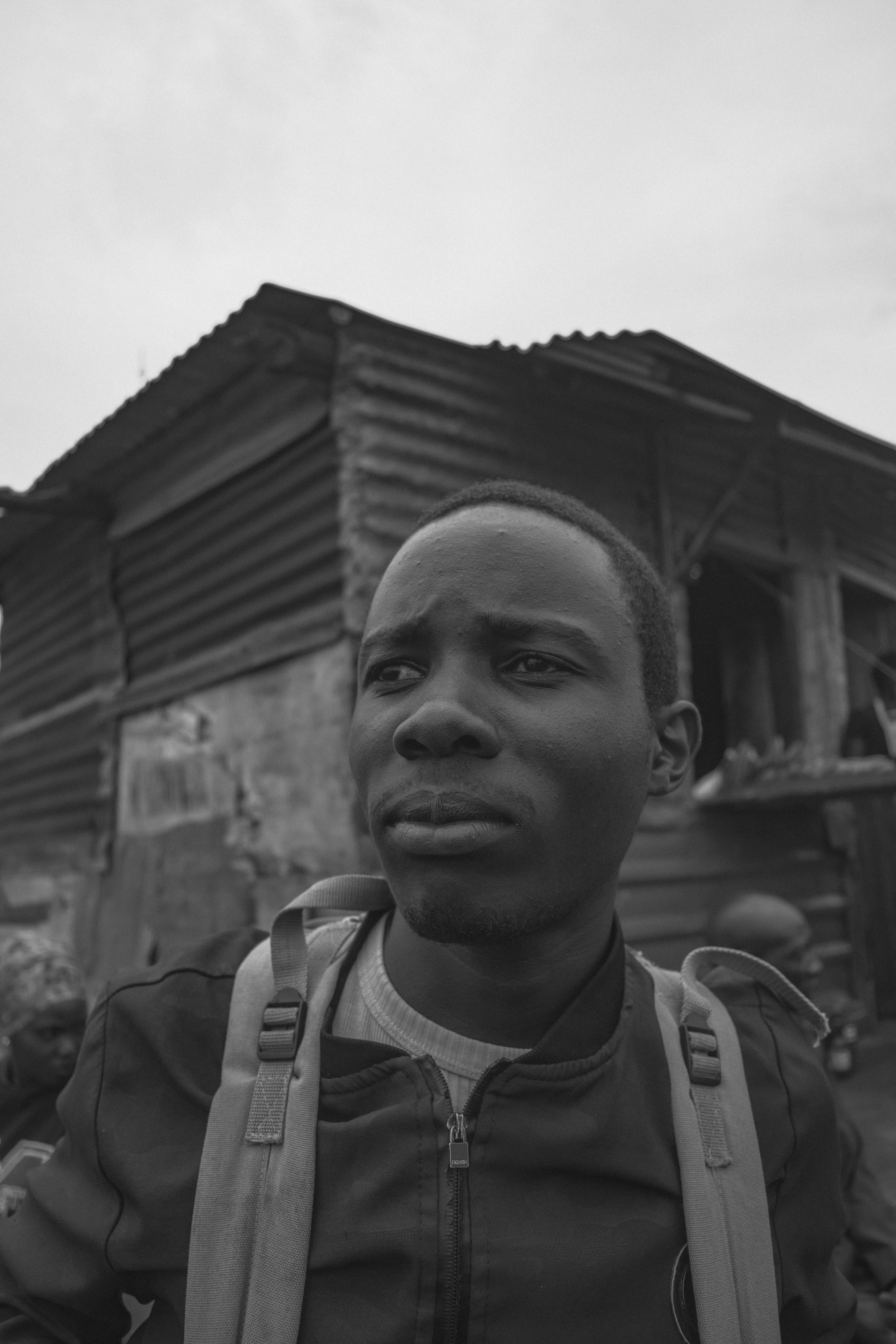 Black and white portrait of a young man looking away from a corrugated metal building