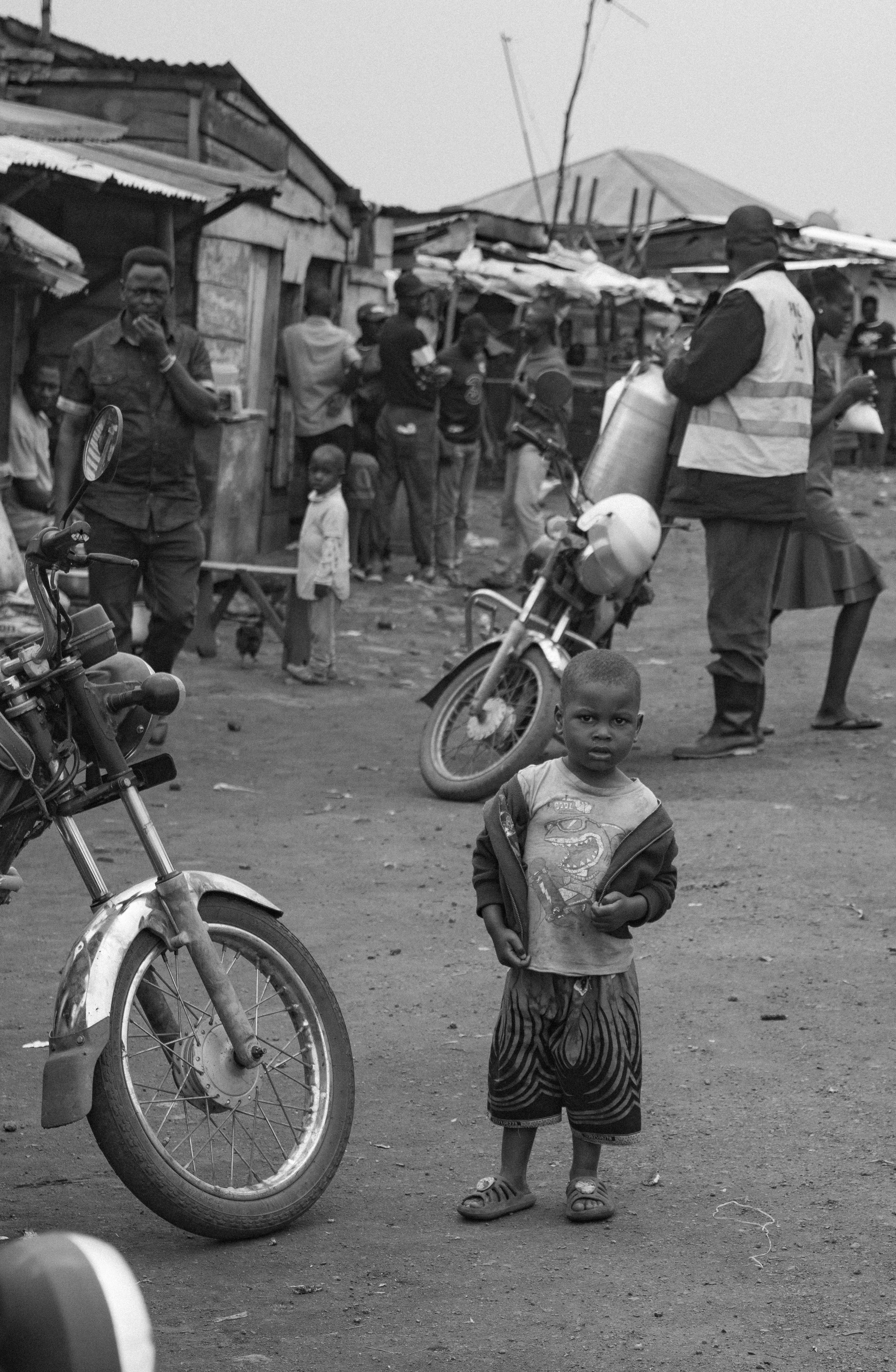 Young boy stands in a dusty street with motorcycles and people in the background