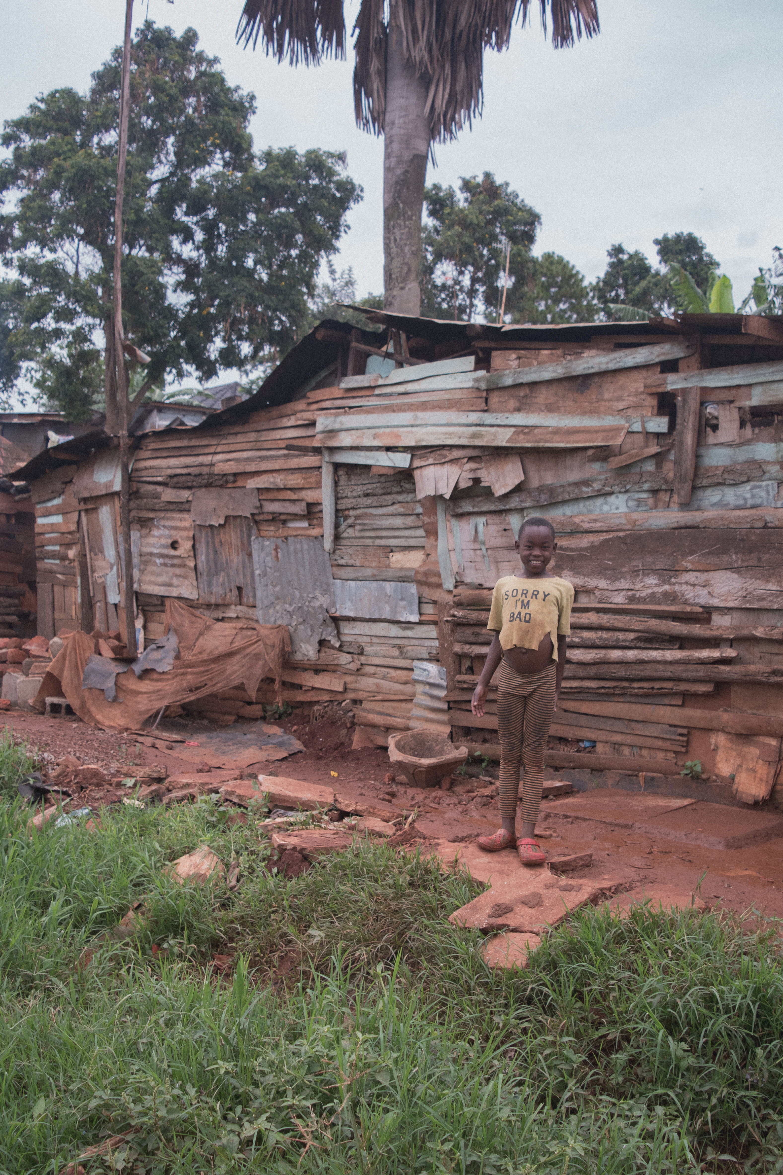 Smiling child stands before a weathered wooden shack in a rural setting