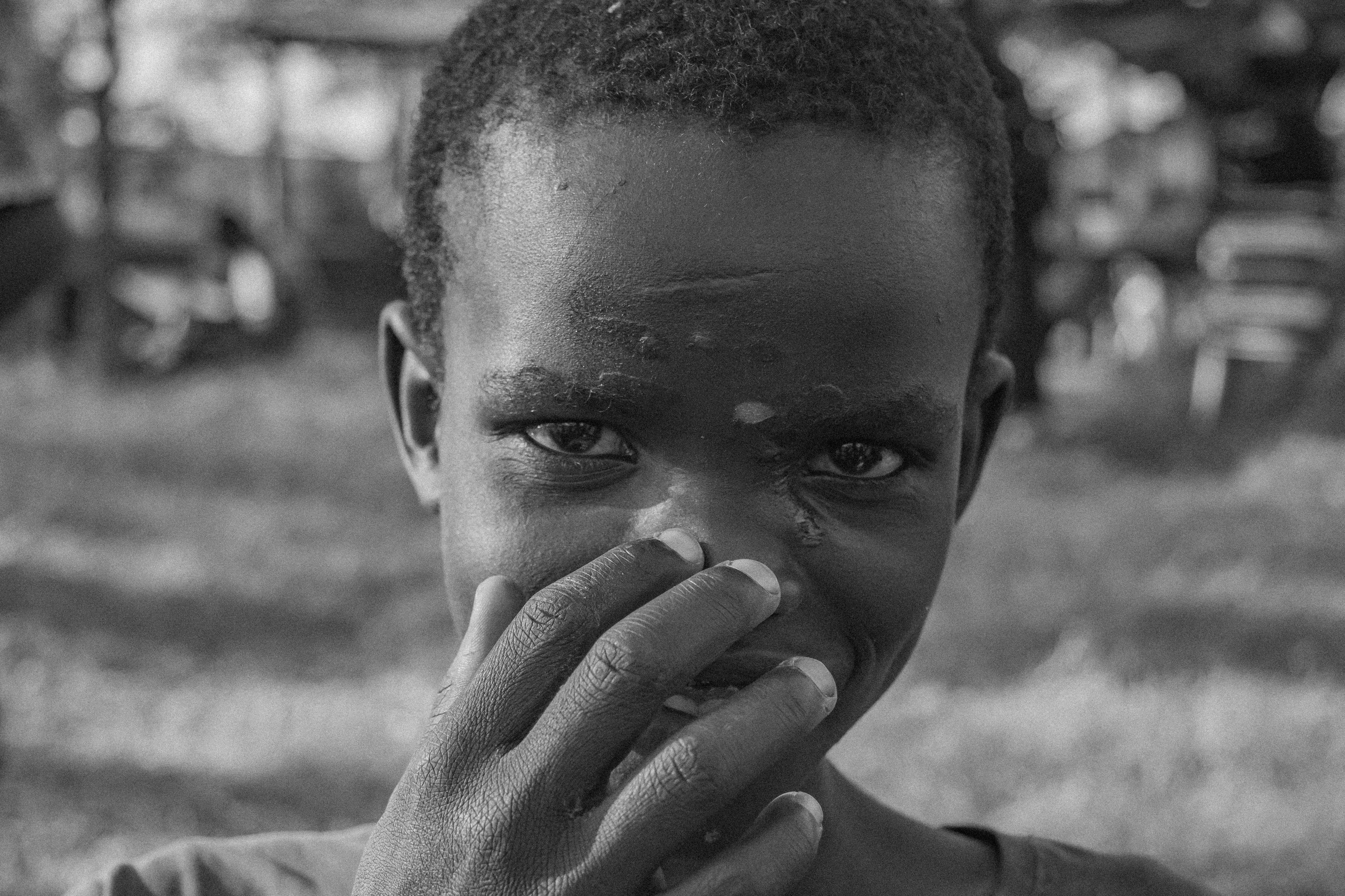 Close-up black and white portrait of a young boy covering his mouth with his hand