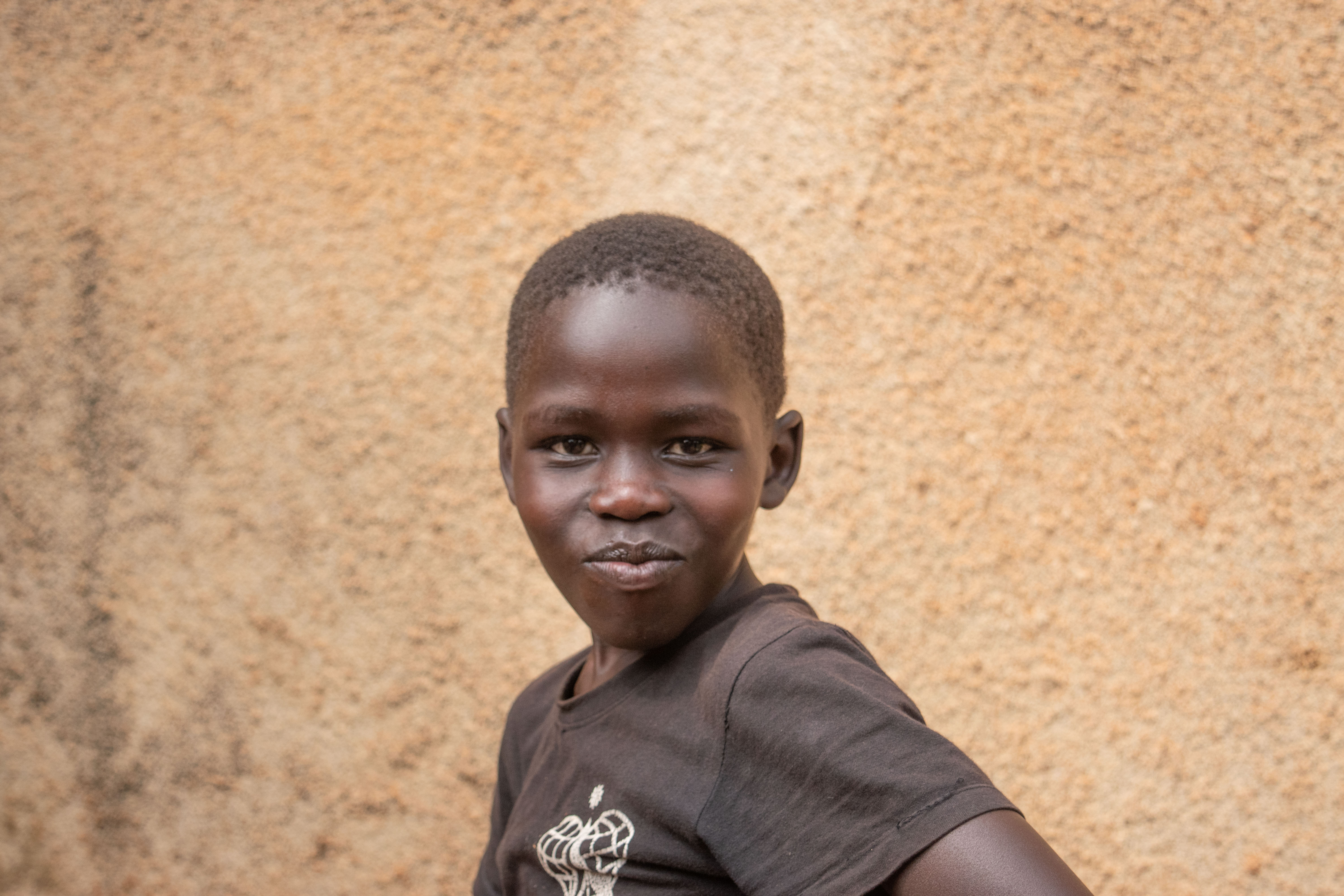Young boy in a dark t-shirt smiles against a textured tan wall